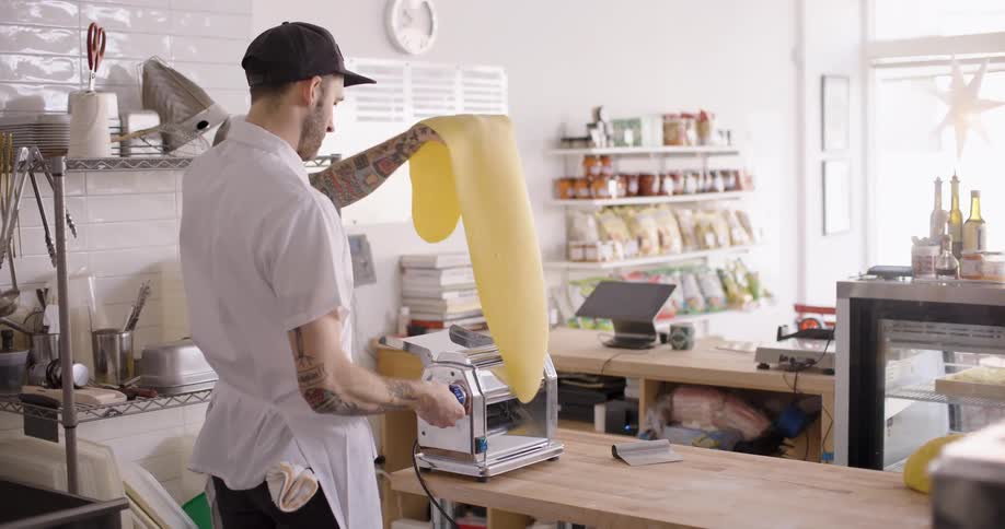 A man passing pasta dough through a machine at the store counter