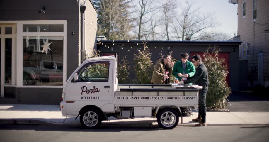 Three men stand around the back of a work truck while eating