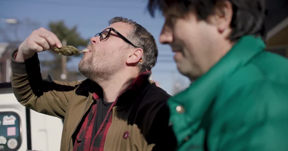 Man shakes head after eating food and smiles with the other man while standing outdoor at midday