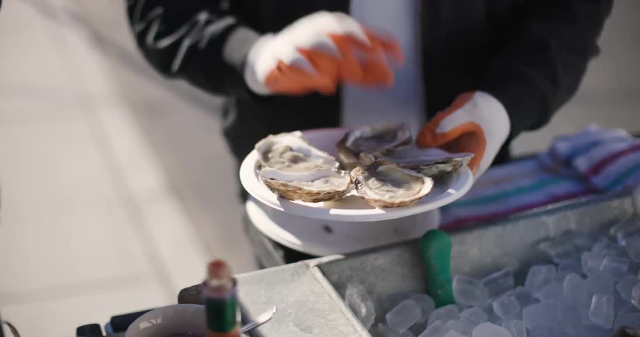 Man standing at street cart at edge of road hands over plated oysters