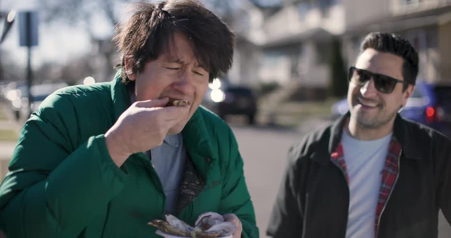 Man eating oyster and his colleagues next to him laughing