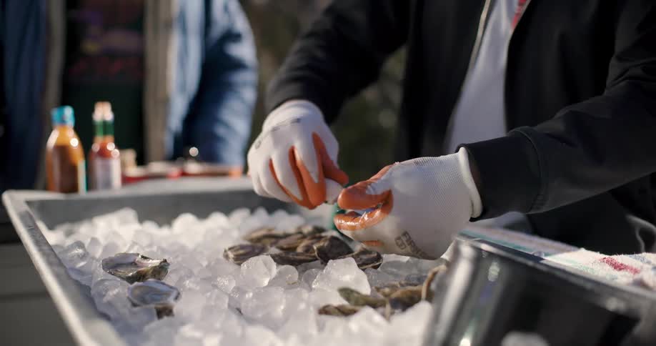 Closeup of the hands of a person with gloves delivering oyster gratin in a food truck to the customer
