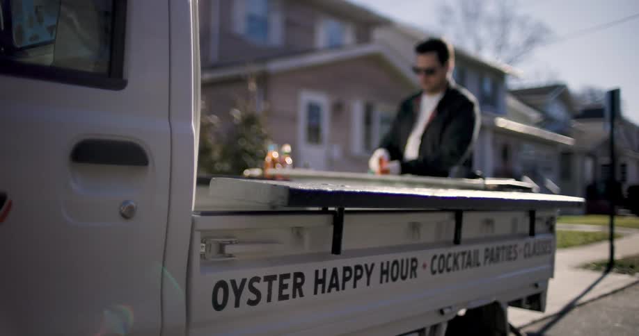 The man is standing behind a little truck with some writing next to him and he is fiddling with something