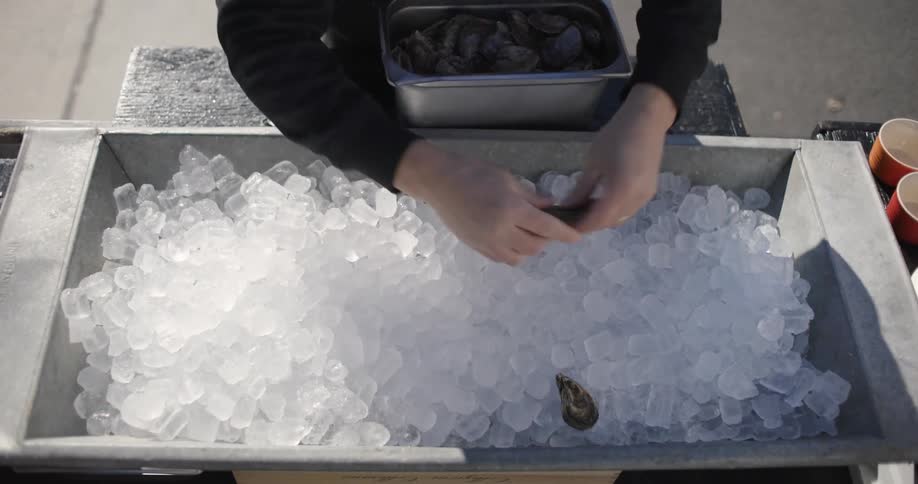 A person placing seafood into a bowl of ice outdoors