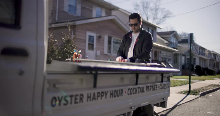 Man standing at back of minitruck parked in residential neighborhood prepares oysters