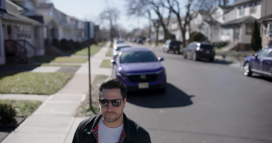 A man standing on the road in a suburb on a sunny day looking around while smiling