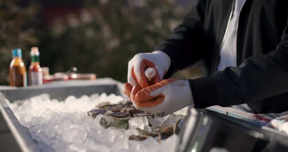 Hands of a person with gloves shucking oysters