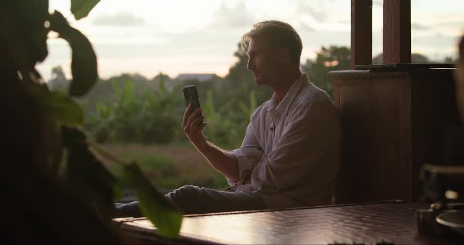 A man talking on his cell phone in a tropical forest at sunset