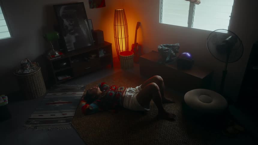 A young Asian woman lying on the living room floor looking thoughtfully at the ceiling