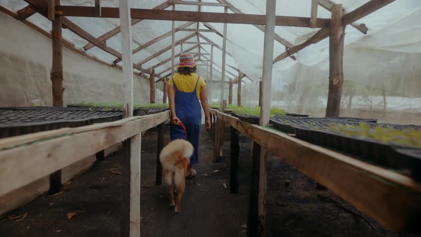 A young asian woman walking a dog through an organic greenhouse