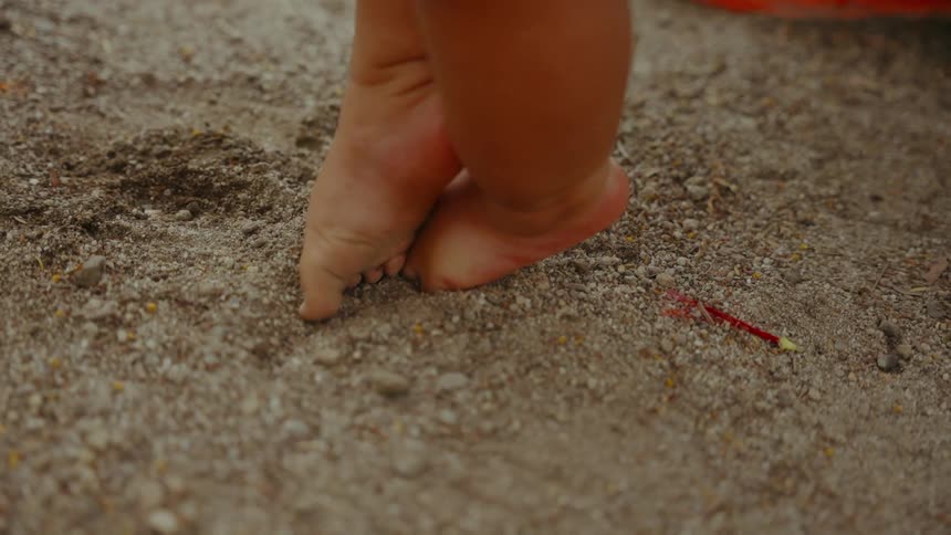 A baby digs its toes into the coarse sand it is standing on