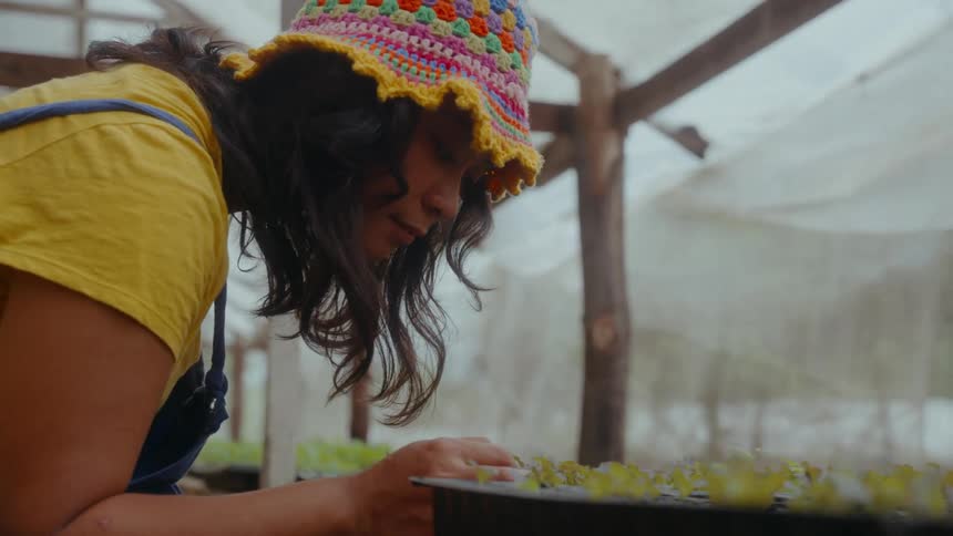 A young Asian woman with a knitted hat touches growing buds inside an organic greenhouse