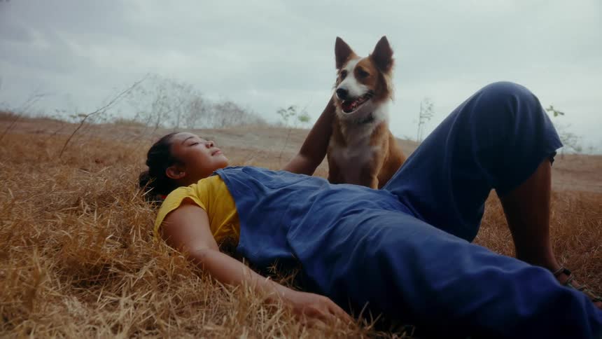 A young Asian woman lies in the grass petting her dog