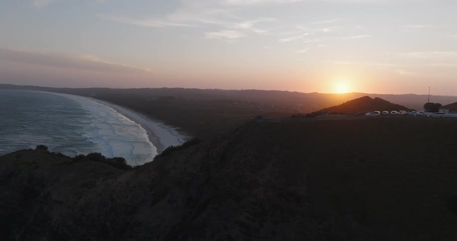 An aerial view of a region with a mountain with a highway and a beach below and in the sky with the sun rising in the morning