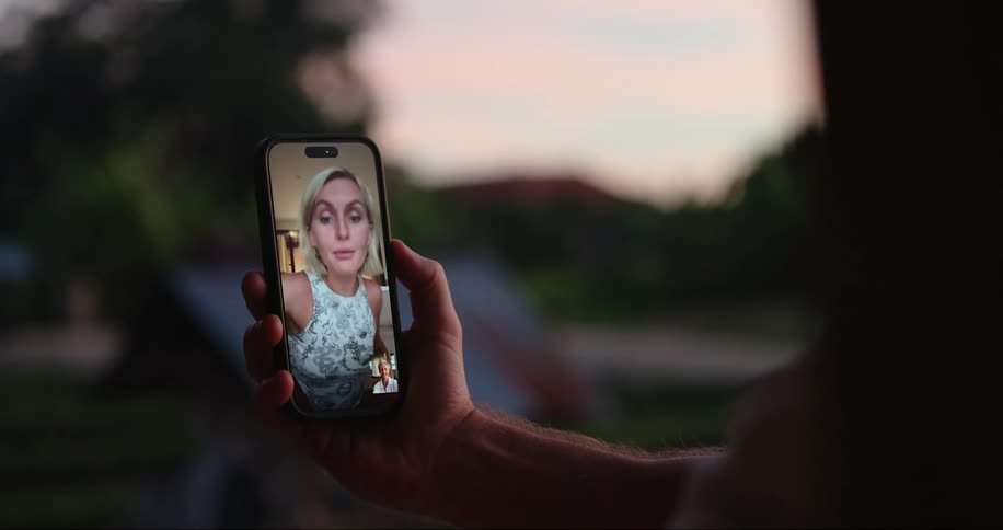 A man on a video call with a woman appears on the cell phone screen