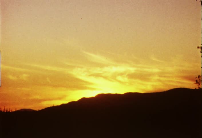 The sun is setting behind a mountain making the sky orange