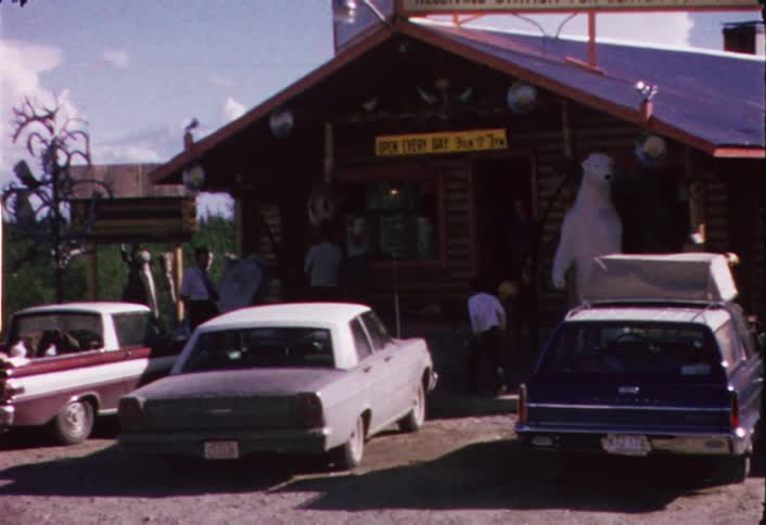 The front of a shop has cars and people in front