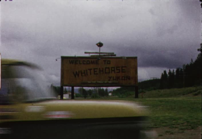 Vintage yellow truck passes  a billboard on a cloudy day