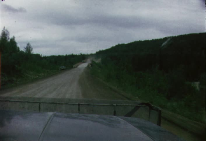 Moving view from a vehicle going down a dirt road as seen through its windshield on a cloudy day