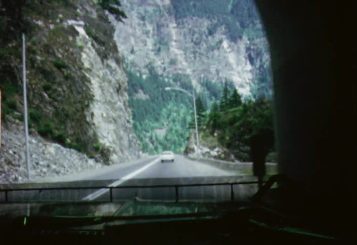 A vehicle driving out of a tunnel on a mountain road during the day