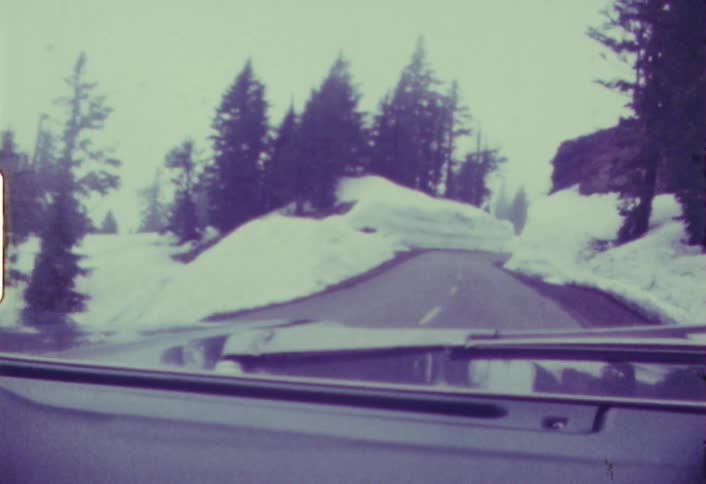 A car is driving down a road in an area heavy with snow