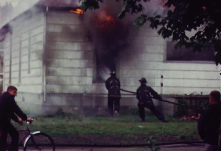 A raging fire burns through a house window as firefighters attempt to extinguish the flames