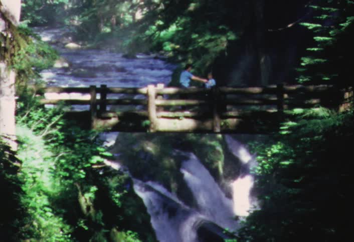 Two people standing on a wooden bridge as a river flows beneath them