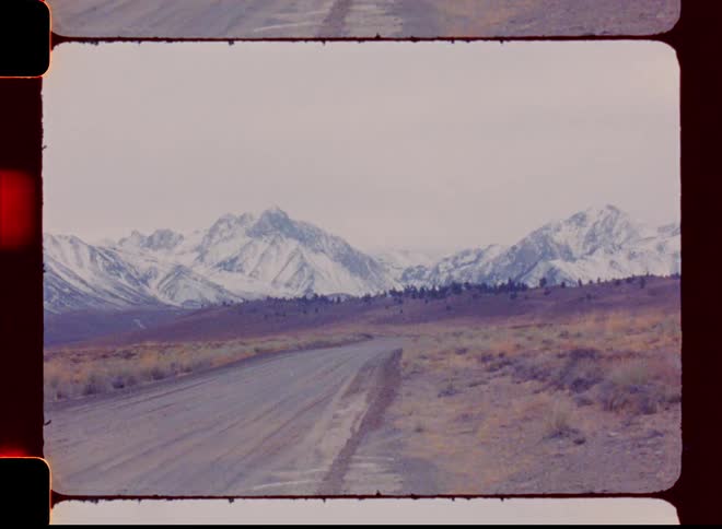 Landscape of a dirt road with a view of snowcovered mountain ranges on a cloudy day