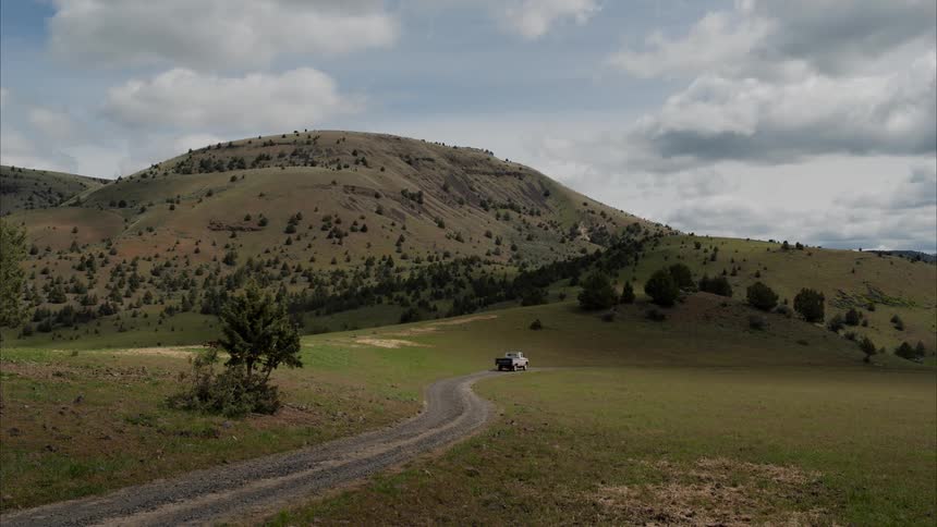 Pickup truck traveling on a street through a landscape with mountains and forests