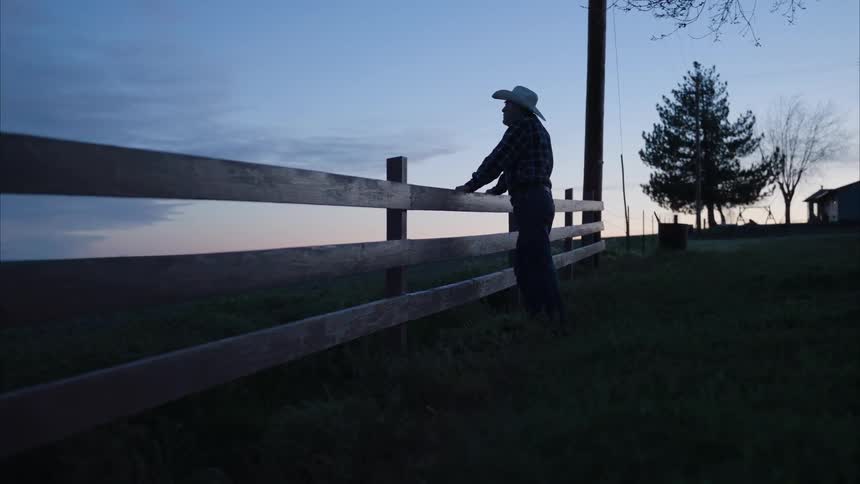 A man on top of a farm fence watching the nightfall