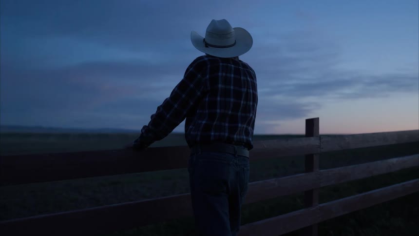 An old man stands against a fence outdoors