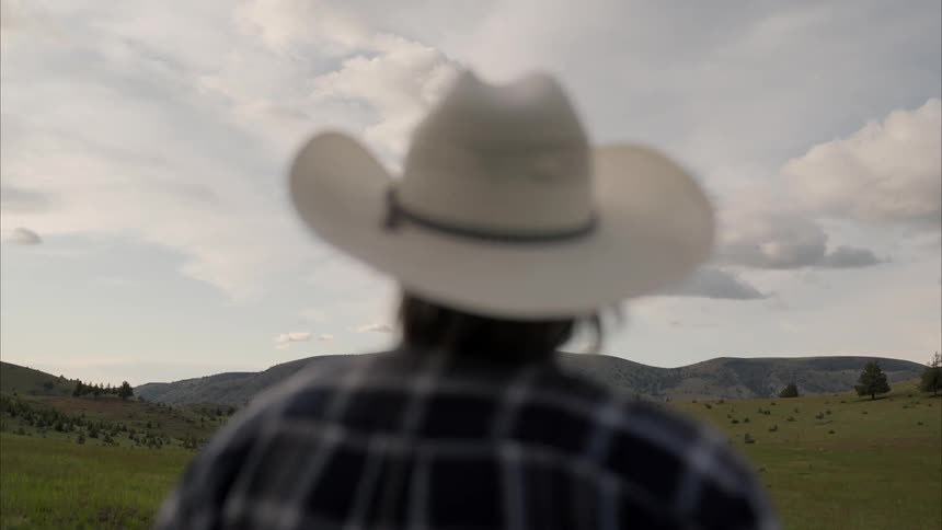 A sad old cowboy stares into the distance then at the grassy plain where hes standing
