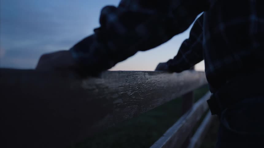 A man standing outdoors with his hands resting on a fence
