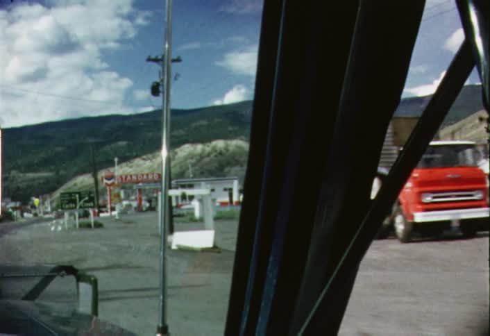 A car passing by parked trucks and a gas station during the day