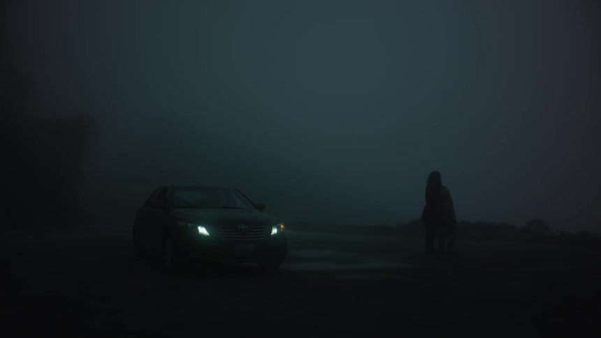 Silhouette of two people hugging in a sawmill at night and next to a vehicle with its headlights on