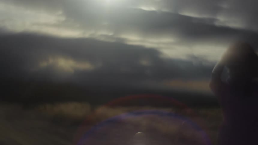 Blurred frame of a woman with her hands on her head in a pasture on a clear day with clouds and sunlight