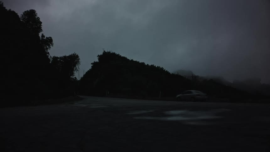 Car passing on a road on the edge of mountains and forests in a late afternoon with the sky with black clouds