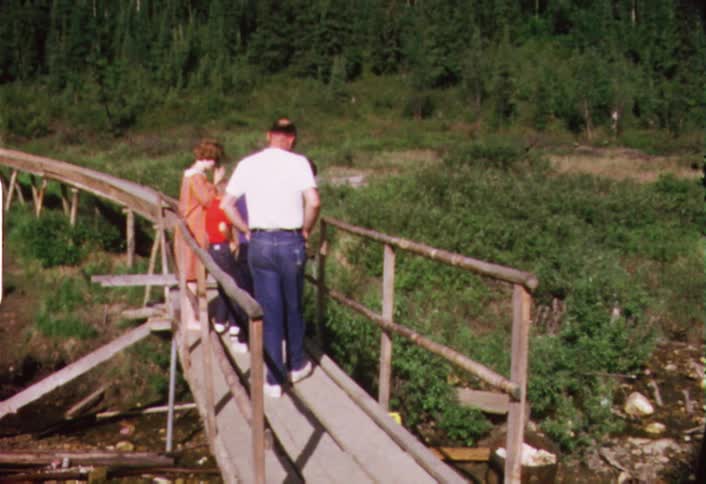 Several people crossing a narrow bridge but stopping to look below them
