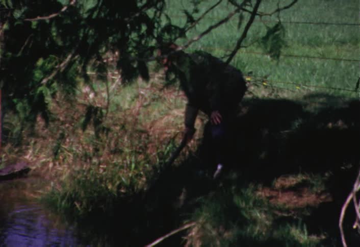 Boy poking a stick at something in a stream