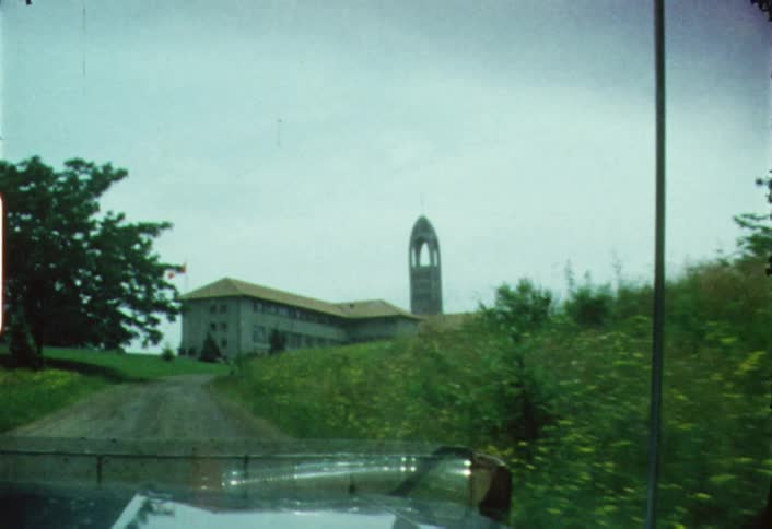 A vehicle is driving toward a large building with a tower during the day
