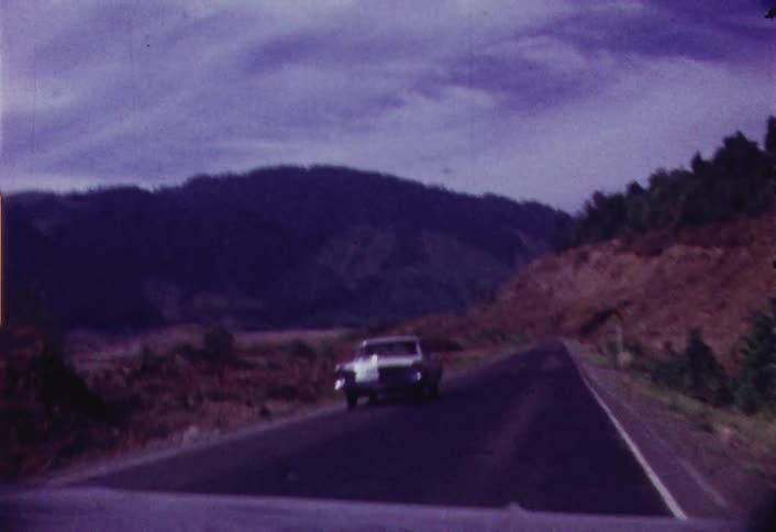 Cars travelling down a road near a rocky hill