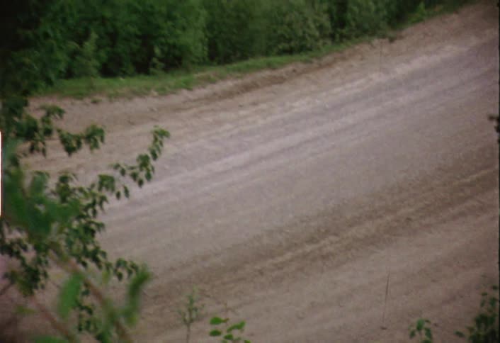 A winding dirt road is empty and surrounded by trees