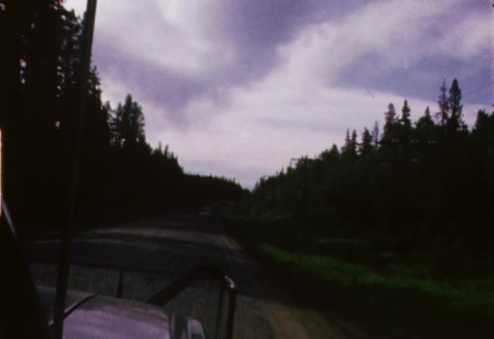 Moving view from a vehicle going down a dirt road as seen through its windshield on a cloudy day