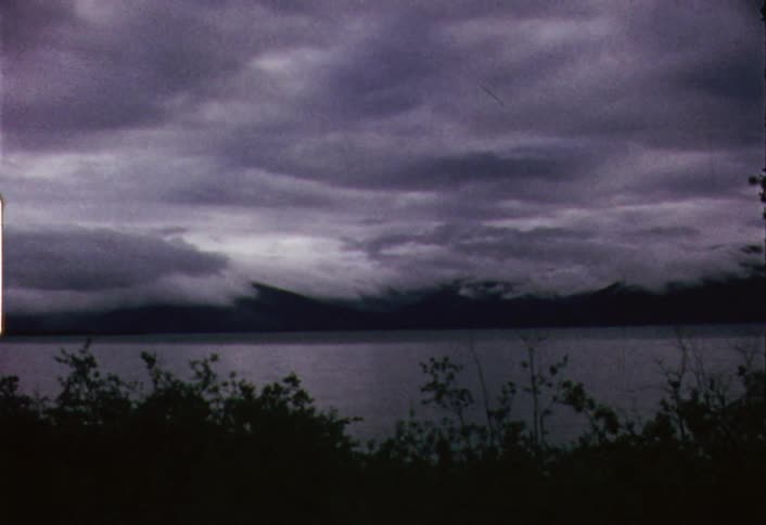 Storm clouds are hovering over mountains and a lake