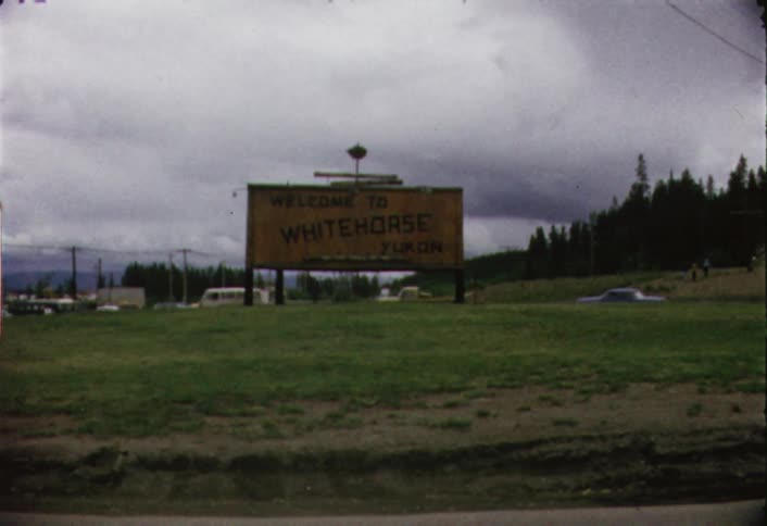 Vehicles travel on a road behind a welcome sign