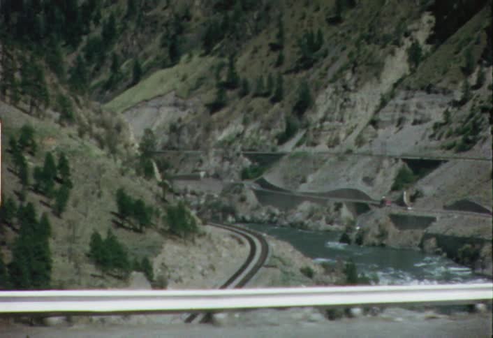 Moving view of a river winding through wilderness with a pair of train tracks on a hill
