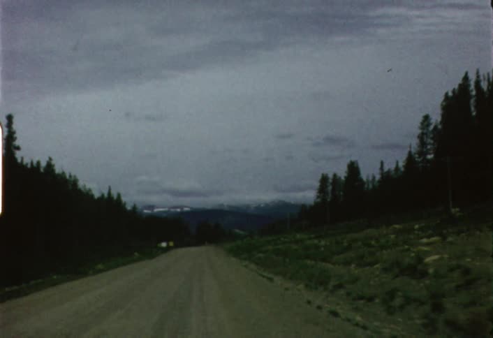 Moving view from a vehicle going down a dirt road as seen through its windshield on a mostly cloudy day