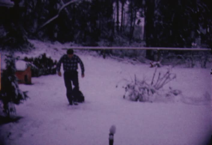 A man is playing with a dog while snow falls around them