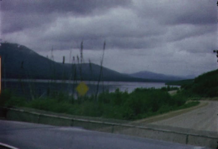 Moving view from a vehicle going down a dirt road as seen through its windshield on a cloudy day