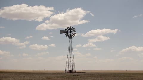 A windmill turning slowly on a barren field
